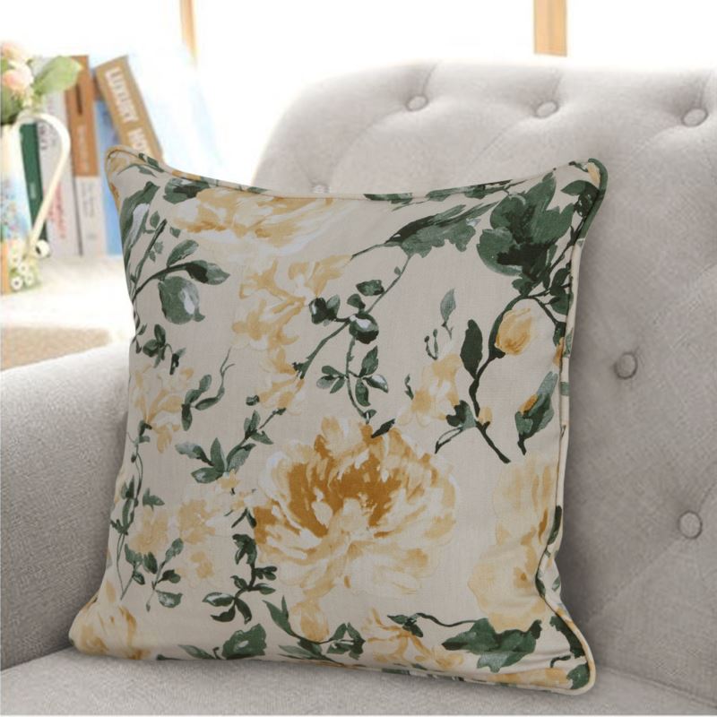 Cushion cover with a pattern of yellow roses and greeery hanging from a silver curtain pole against a grey couch