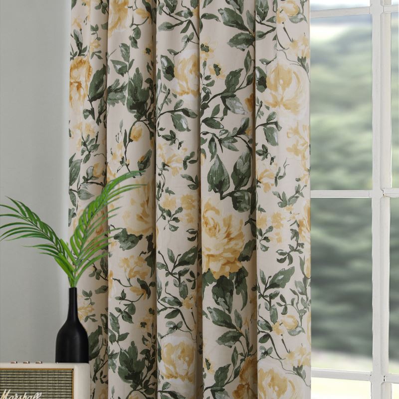 Close up of curtains with a pattern of yellow roses and greeery hanging from a silver curtain pole against a white wall